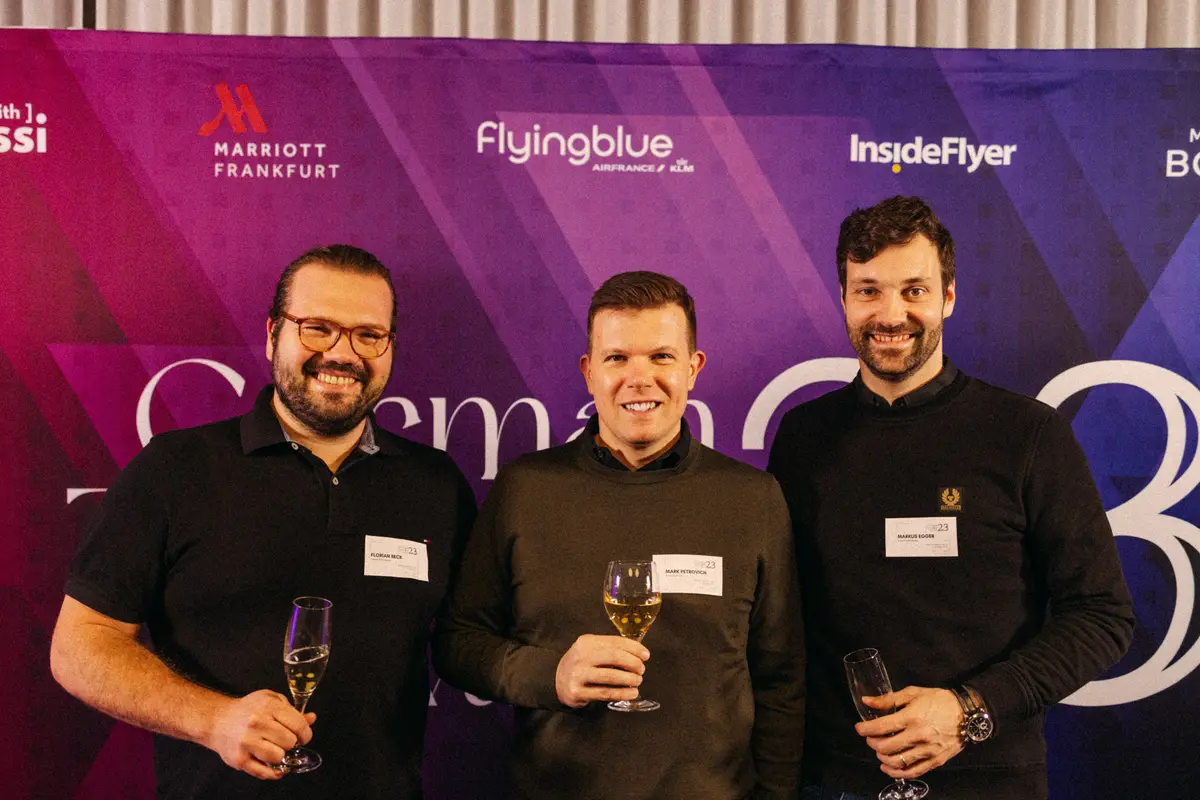 Three guests with glasses in front of the awards wall